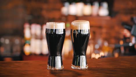 Two-glasses-of-dark-stout-beer-covered-with-foam,-standing-on-the-counter-in-a-pub