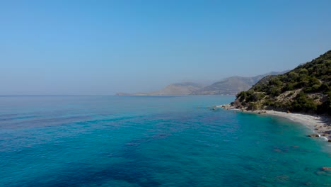 Blue-azure-sea-water-on-shoreline-of-Mediterranean,-calm-emerald-lagoon-washing-mountains