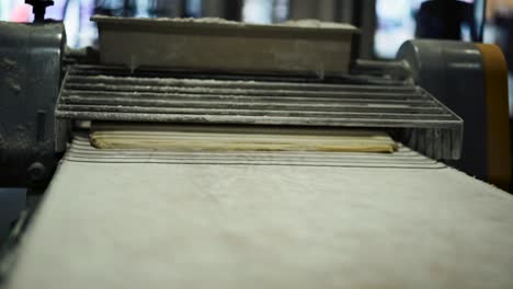 wide-close-up-shot-of-slab-roller-and-sheet-of-laminated-croissant-dough-coming-out-of-the-conveyor-belt