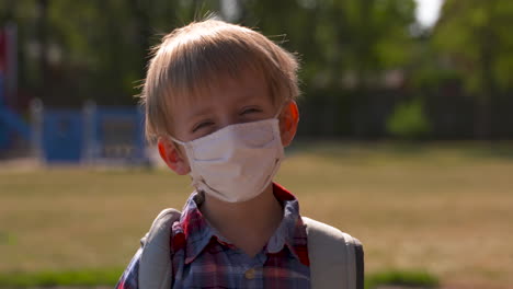 Portrait-of-a-little-boy-wearing-a-face-mask-in-a-school-yard