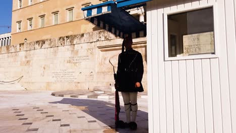 Greek-presidential-guard-with-traditional-military-uniform,-evzone,-is-preparing-for-the-ceremonial-guard-change-in-front-of-the-Hellenic-Parliament,-while-holding-red-rifle