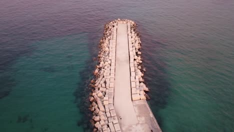 Aerial-view-of-stony-jetty-surrounded-by-crystal-clear-ocean-water-during-sunset