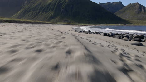 Aerial-shot-flying-very-close-to-the-sand,-revealing-waves-crushing-in-on-the-beach-and-a-mountain-in-the-background