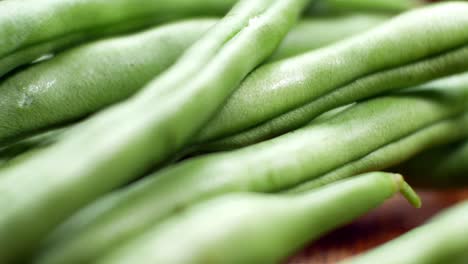 Raw-fresh-uncooked-string-beans-on-wooden-kitchen-surface-close-up-selective-focus