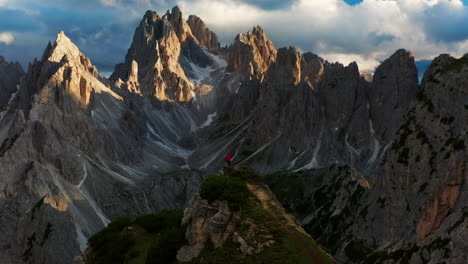 Jagged-peaks-of-Dolomites,-Man-stands-alone-on-cliff,-Italy