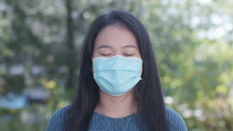 Asian-American-young-woman-wearing-a-face-mask-outdoors,-close-up