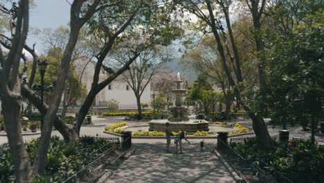 Drone-aerial-flying-low-on-a-beautiful-park-with-a-fountain-in-Antigua-Guatemala,-Central-America