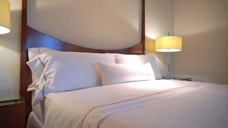 Pan-from-the-bedside-table-and-lamp-across-a-bed-and-wooden-headboard-to-the-other-side-of-the-hotel-suite-room