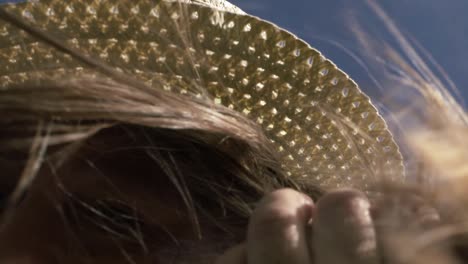 Woman-holding-onto-straw-hat-on-windy-day-with-hair-blowing-close-up-shot