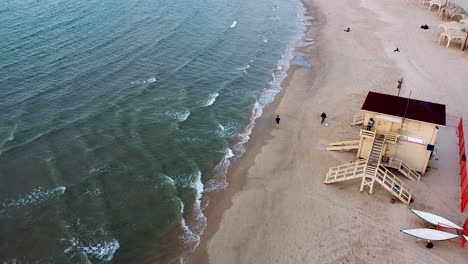 Aerial-long-shot-follow-man-running-at-the-beach,-lifeguard-stand,-drone-shot