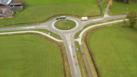 Drone-view-above-road-roundabout-bird-eye-shot-of-trucks,-motorbikes-between-lush-green-fields