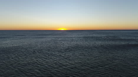 Aerial-view-of-the-sun-rising-in-the-horizon-over-a-calm-moving-ocean,-at-the-popular-Burleigh-Heads-Gold-Coast-QLD-Australia