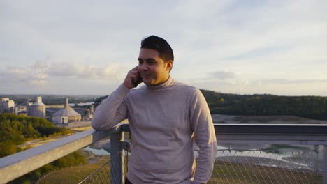 A-young-man-in-a-turtle-neck-sweater-calling-on-the-phone-on-top-of-a-mountain