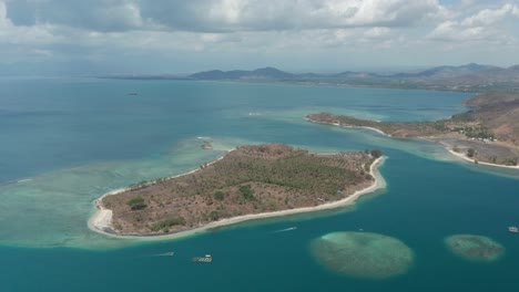 Remote-island-Gili-Sudak-with-pristine-blue-water-surrounding-its-shore,-aerial