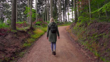 Hiking-Girl-walking-a-trail-in-a-beautiful-forest-with-her-raincoat-and-backpack-on