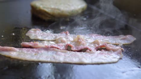 cooking-slices-of-bacon-on-a-grill-next-to-a-burger-in-fast-food-restaurant-slow-motion
