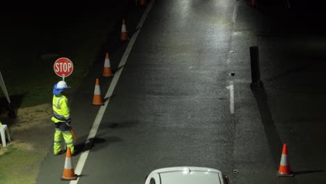 Traffic-Guard-Holding-Slow-Sign-And-LED-Traffic-Wand-Directing-Cars-Travelling-At-Night---NSW-QLD-Border-During-COVID-19---Gold-Coast,-Australia