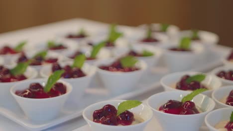 Close-up-of-many-cups-of-cherry-compole-with-peppermint-leaves-presented-in-white-china-cups-at-a-buffet
