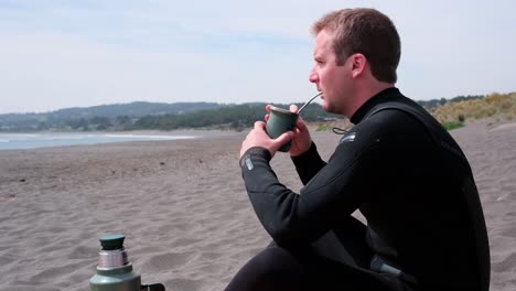 man-drinking-Argentine-Mate-drink-on-the-beach-after-a-surf-session-in-Chile-Pichilemu-punta-de-lobos-on-a-sunny-day-and-wearing-a-wetsuit
