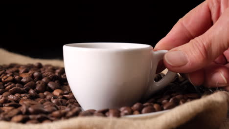 Frauenhand,-Die-Kaffeetasse-Auf-Kaffeebohnen-Und-Jute-Legt