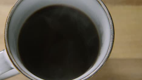 Pfanne-Ließ-Eine-Dampfende-Tasse-Schwarzen-Kaffee-Auf-Einem-Holztisch-Stehen,-60fps
