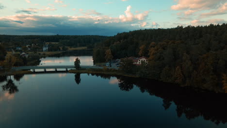 Aerial-dolly-shot-of-natural-lake-surrounded-by-forest-and-small-village-Kowalskie-Blota-in-Poland