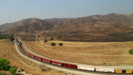 Train-moving-slowly-along-the-tracks-beneath-an-extinguished-wildfire-burn-near-Caliente,-California