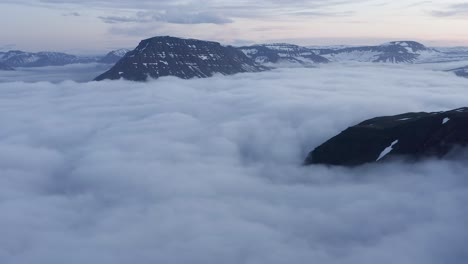 Magnificent-view-of-fjord-covered-in-low-clouds-and-large-mountain-peaks,-aerial