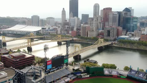 Aerial-pullback-reveals-PNC-Park,-Pittsburgh-Pirates-Major-League-Baseball-team-with-Roberto-Clemente-bridge-and-urban-city-downtown-skyline