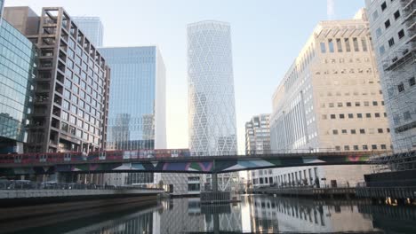 Red-London-DLR-train-passing-over-bridge-behind-Newfoundland-building-Canary-wharf-London