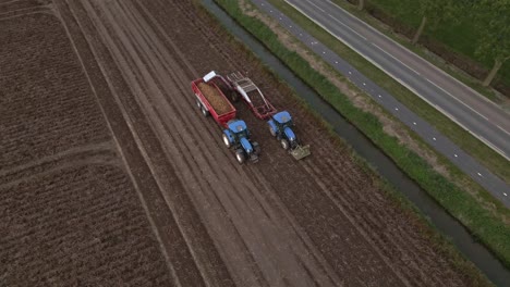 Drone-circle-around-tractors-driving-over-farm-land-harvesting-potato-crop