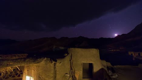 Old-Village-House-at-Night-and-Moon-and-Stars-and-Orion-Nebula-sets-Over-the-Mountains-in-Background-Landscape