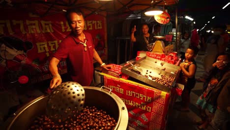 Ein-Straßenverkäufer,-Der-Geröstete-Kastanien-Umrührt,-Während-Kunden-Auf-Einem-Traditionellen-Offenen-Nachtmarkt-In-Thailand-Warten