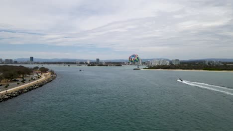 Aerial-view-of-a-fast-boat-pulling-a-parasail-through-the-air-with-a-city-skyline-in-the-background