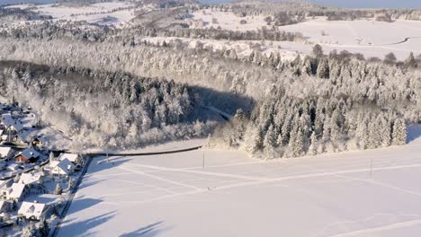 Drone-flight-over-a-winter-landscape-with-a-little-town-left-sided,-smooth-flight-going-slowly-down