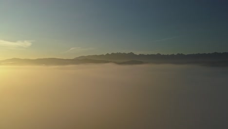 Aerial-above-mist-during-colorful-sunrise-with-mountain-peaks-in-distance