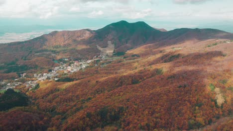 Spectacular-drone-footage-of-Japanese-mountains-in-fall-colours-with-cloud-shadows-over-village,-Zaoonsen-in-Japan,-aerial-shot