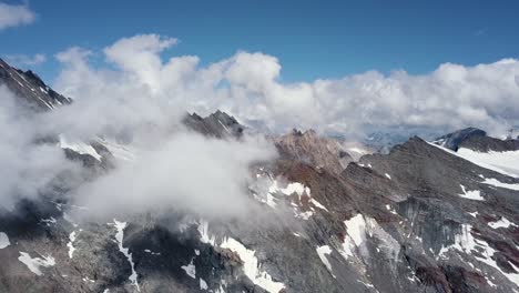 Aerial-Dolly-Aus-Einer-Bergkette-über-Den-Wolken-An-Einem-Sonnigen-Sommertag-Mit-Schneeflecken