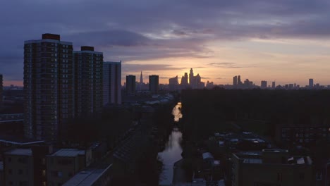Low-dolly-forward-Aerial-drone-shot-of-London-Canal-Victoria-park-towards-city-skyline-at-sunset