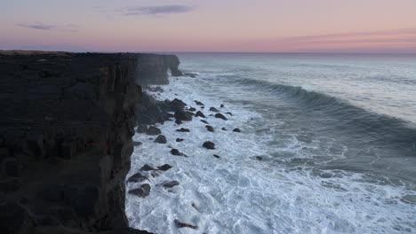 White-ocean-waves-splashing-on-the-rocky-cliff-at-sunset--wide