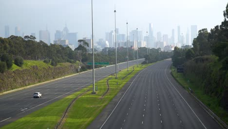 Car-drives-down-an-eerily-empty-highway-during-the-COVID-19-lockdown---shot-in-Melbourne,-Australia,-but-can-represent-many-city-skylines-and-the-impact-of-coronavirus-around-the-world