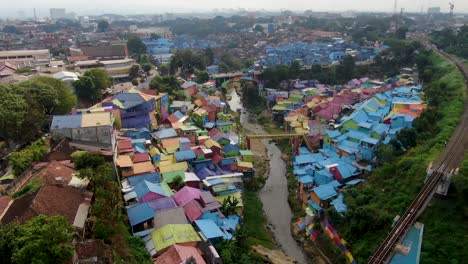 Railway-bridge-and-Jodipan-rainbow-village-in-Malang,-Java-Indonesia-aerial-dolly-in