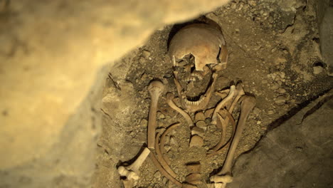 Human-skull-and-bones-in-dirt-Archeology-discovery-in-cave,-Panning-shot
