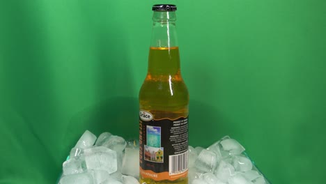 3-3-Glasflasche-Mit-Kola-Champagnergeschmack-Der-Marke-Grace,-Die-Sich-In-Einer-Mit-Eis-Gefüllten-Schüssel-Vor-Einem-Grünen-Bildschirm-Um-360-Grad-Dreht