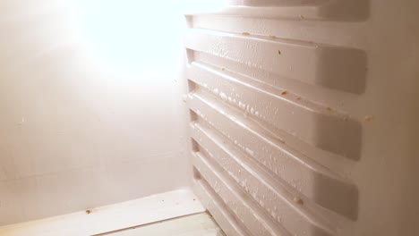 Mann-Mit-Lila-Gummihandschuhen-Reinigt-Die-Seiten-Eines-Schmutzigen-Kühlschranks-Und-Legt-Fensterreiniger-Darauf