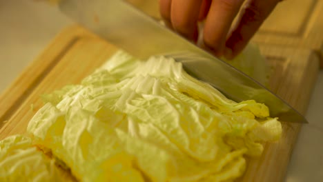 The-cook-chops-fresh-napa-cabbage-on-wooden-kitchen-board-with-steel-chief-knife,-handheld-close-up-shot