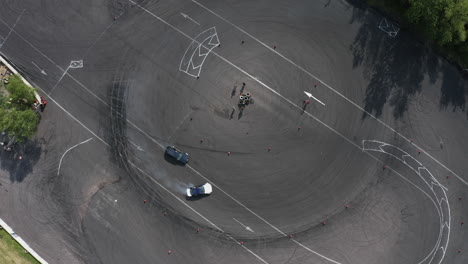 Top-down-aerial-shot-of-two-sport-cars-drifting-in-circle-on-asphalt