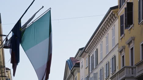 Italienische-Flagge,-Die-An-Einem-Sonnigen-Tag-Mit-Dem-Wind-In-Der-Nähe-Von-Wohngebäuden-Weht