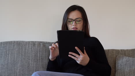 Handheld-shot-of-a-young-woman-using-a-tablet-sitting-on-a-couch