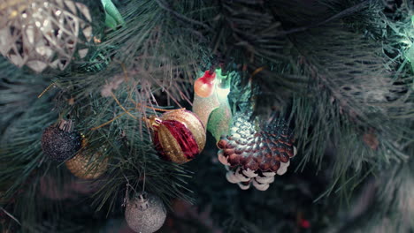 Frosted-Pine-Cone-And-Glittered-Baubles-Hanging-On-Needles-Of-Christmas-Tree---Closeup,-Tilt-Down-Shot